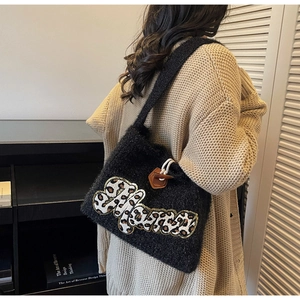 Detail of black knitted tote bag featuring leopard letter patch and wooden horn buckle