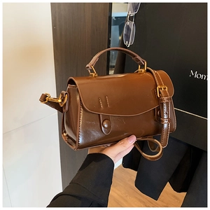 Detail view of glossy brown vintage crossbody bag with gold metal hardware and top handle