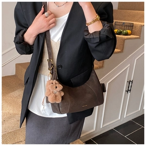 Detail of dark brown dumpling bag with gold logo and cute bear charm on model