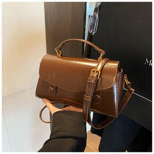 Close-up of a dark brown glossy leather handbag with round buckle details and top handle
