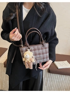 Detail of brown plaid bucket bag with leather handles and a cute plush bear charm