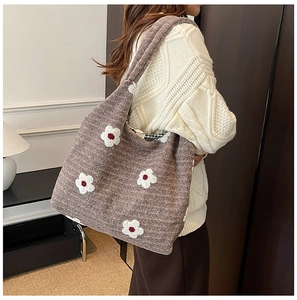 Detail of a brown knitted tote bag with floral pattern shown on a shoulder in a cozy room