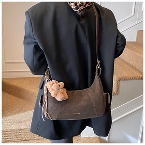Close-up of brown suede underarm bag with cute plush bear and tassel detail