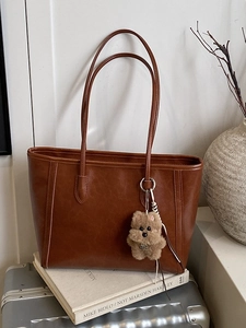 Caramel glossy tote bag with dog plush charm on a silver suitcase for autumn fashion