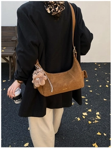 Brown faux suede crescent bag with plush bear charm against autumn ginkgo leaves