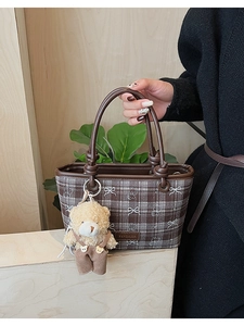 Detail of vintage brown plaid bucket bag featuring a bear charm and elegant knot strap details