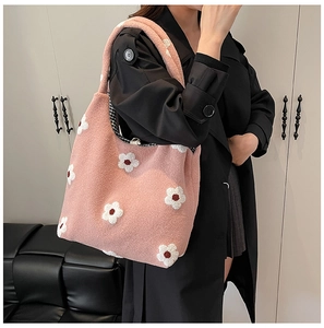 Pink plush tote bag with white flower charms shown on a model in a black coat
