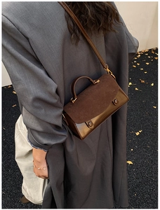 Brown vintage style handbag with suede flap and dual strap shown in outdoor setting