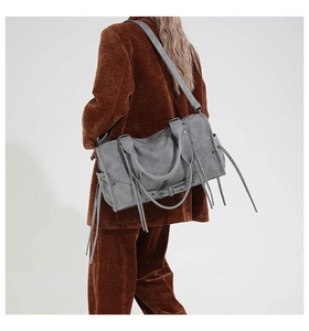 Detailed view of grey vintage leather shoulder bag with tassels and rivets on a model