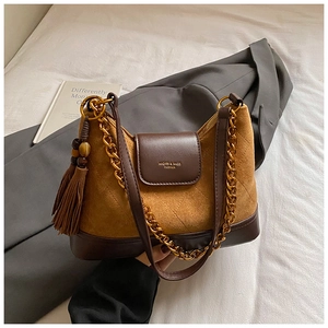 Detail of a brown suede handbag with a gold chain, leather strap, and tassel pendant
