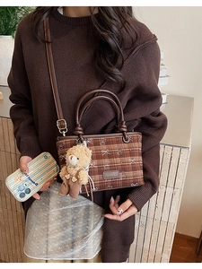 Detail of a brown plaid bucket bag with a plush bear charm and leather handle
