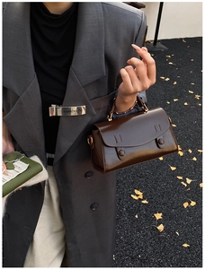 Top view of a dark brown glossy vintage handbag held by a model in autumn street style
