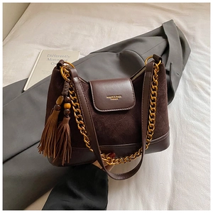 Detail of dark brown suede shoulder bag featuring a gold chain and beaded tassel accent