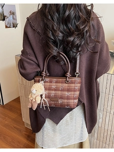 Detail of a brown plaid bucket bag featuring a bear print and a cute teddy bear pendant