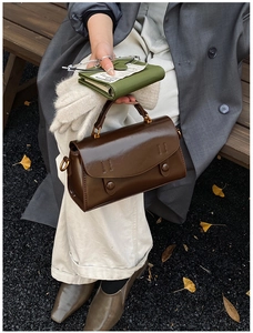 Close-up of brown faux leather handbag with double decorative buckles on an outdoor bench