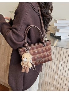 Detail view of a brown plaid bucket bag with bear pendant and leather trim