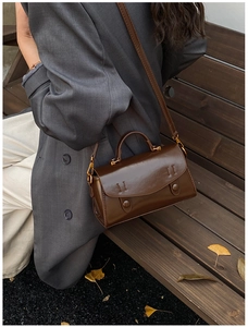 Retro brown leather crossbody bag shown on a model sitting on a wooden bench outdoors