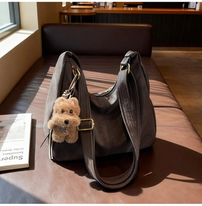 Dettaglio di una borsa tote in pelle con ciondolo a orsetto su un divano in pelle vintage