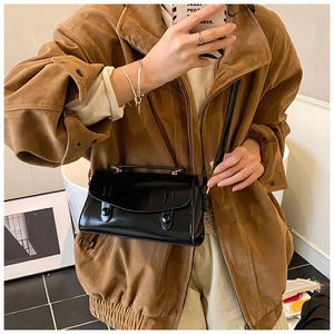 Close-up of a glossy black patent leather square bag worn as a stylish crossbody bag