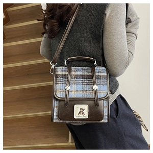 Detail view of British plaid fabric and brown leather stitching on a vintage backpack