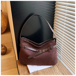 Detailed view of dark brown suede hobo bag with eyelet belt strap on a vintage book