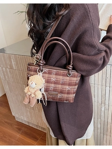 Rear view of a model wearing a brown checkered bucket bag with a cute bear charm pendant