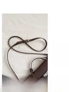Detail of adjustable shoulder strap with silver buckle on dark brown leather handbag