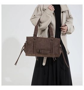 Close-up of retro brown suede tote with long tassels and metallic buckle detailing