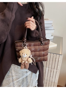 Brown plaid bucket bag with teddy bear charm and brand logo in a cozy home setting