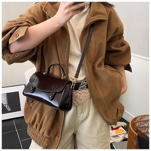 Close-up of a glossy dark brown leather crossbody bag with vintage metal clasp detail