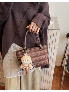 Detailed view of a brown plaid bucket bag with a plush bear charm and leather handle