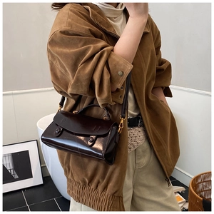 Brown glossy leather handbag with gold metal hardware worn as a crossbody bag