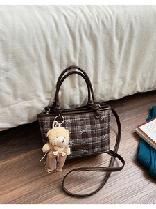 Detail of a brown plaid bucket bag with plush bear charm and leather strap