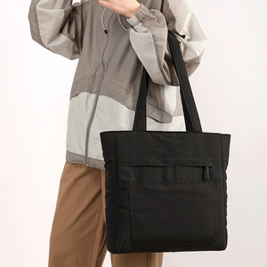 Detailed view of black nylon tote bag with front zipper pocket on female model