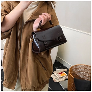Detail of dark brown glossy leather handbag held by model in a modern home setting