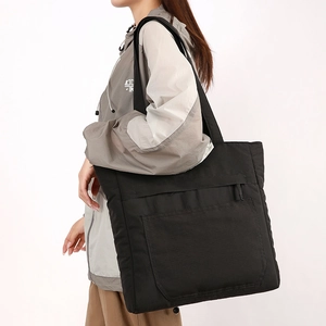 Side view of a large black waterproof nylon tote bag with functional front pockets on a model