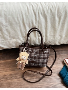 Detailed view of brown checkered bucket bag with cute bear charm in cozy home setting