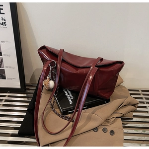 Close-up of wine red patent leather tote bag with baseball bat charm on a metal bench