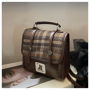 Close-up of British plaid fabric and bear embroidery on the retro brown leather backpack