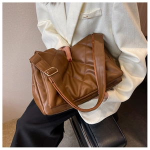 Detail der tiefbraunen Stepptasche mit breitem Gurt auf einem weißen Blazer-Outfit