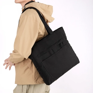 Detailed side view of a large black waterproof nylon tote bag worn by a male model