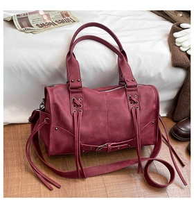 Detail of vintage burgundy tote bag with metal rivets and decorative fringe tassels