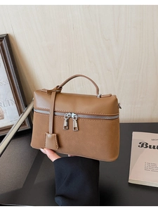 Detail of a brown grain leather handbag with silver double zippers and top handle