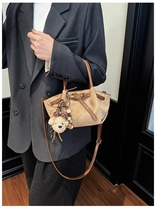 Detail of tan suede tote with leather straps and cute bear charm in dark studio