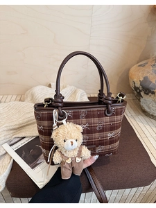Close-up of brown plaid bucket bag with bear print and plush toy charm on wooden desk