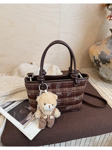 Detail of a brown plaid bucket bag featuring a teddy bear charm and logo lettering