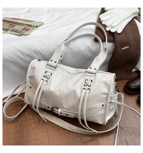 Detail of white Boston bag featuring metallic eyelets and long tassel decorative accents
