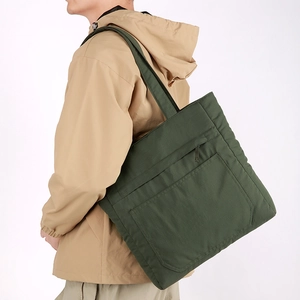 Side view of olive green waterproof nylon tote bag with front pocket worn by a model