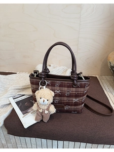 Detail of vintage brown plaid bucket bag with cute teddy bear charm on white knitwear