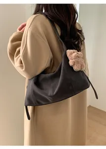 Détail du sac hobo en daim gris avec surpiqûres et pendentif ours sur un manteau beige